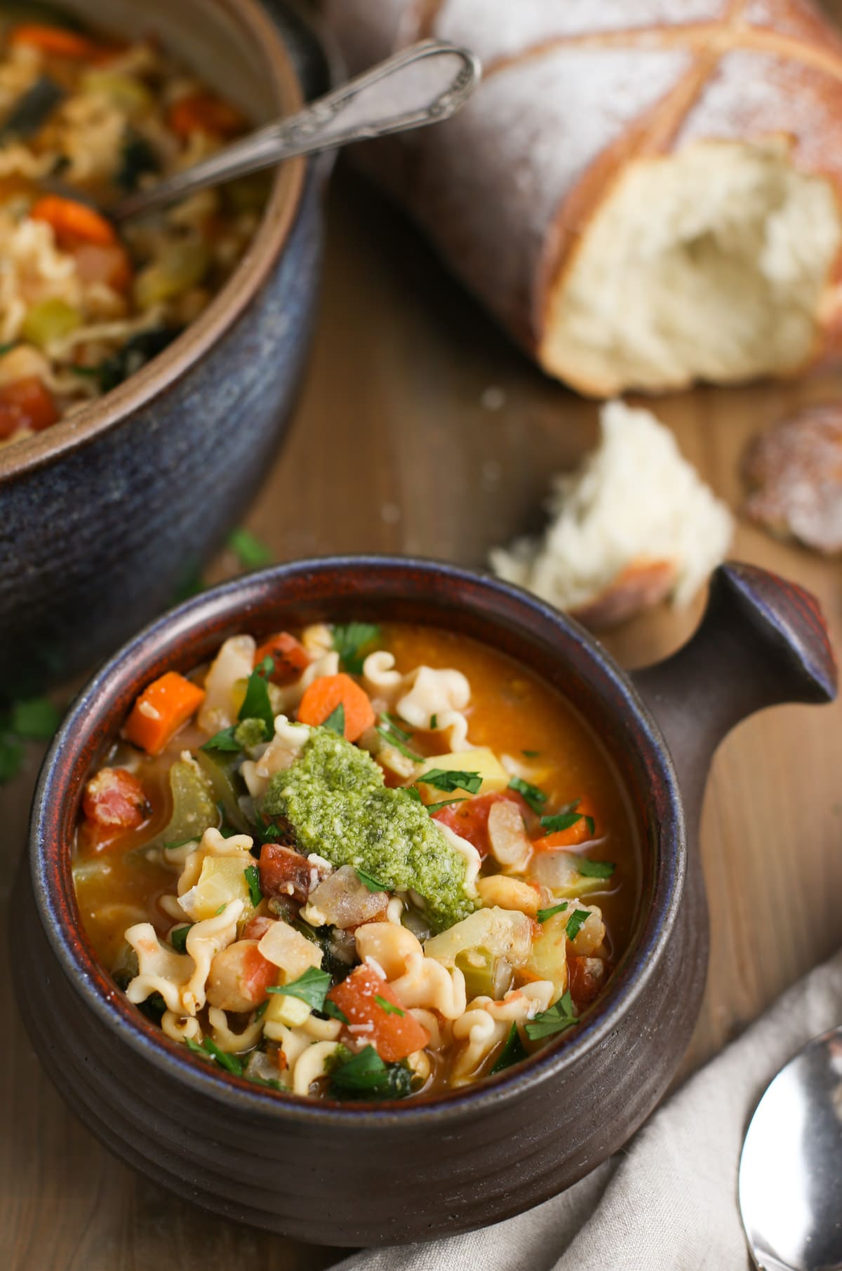 Mighty Minestrone bowl topped with basil pesto and fresh Parmesan cheese with torn bread pieces in background